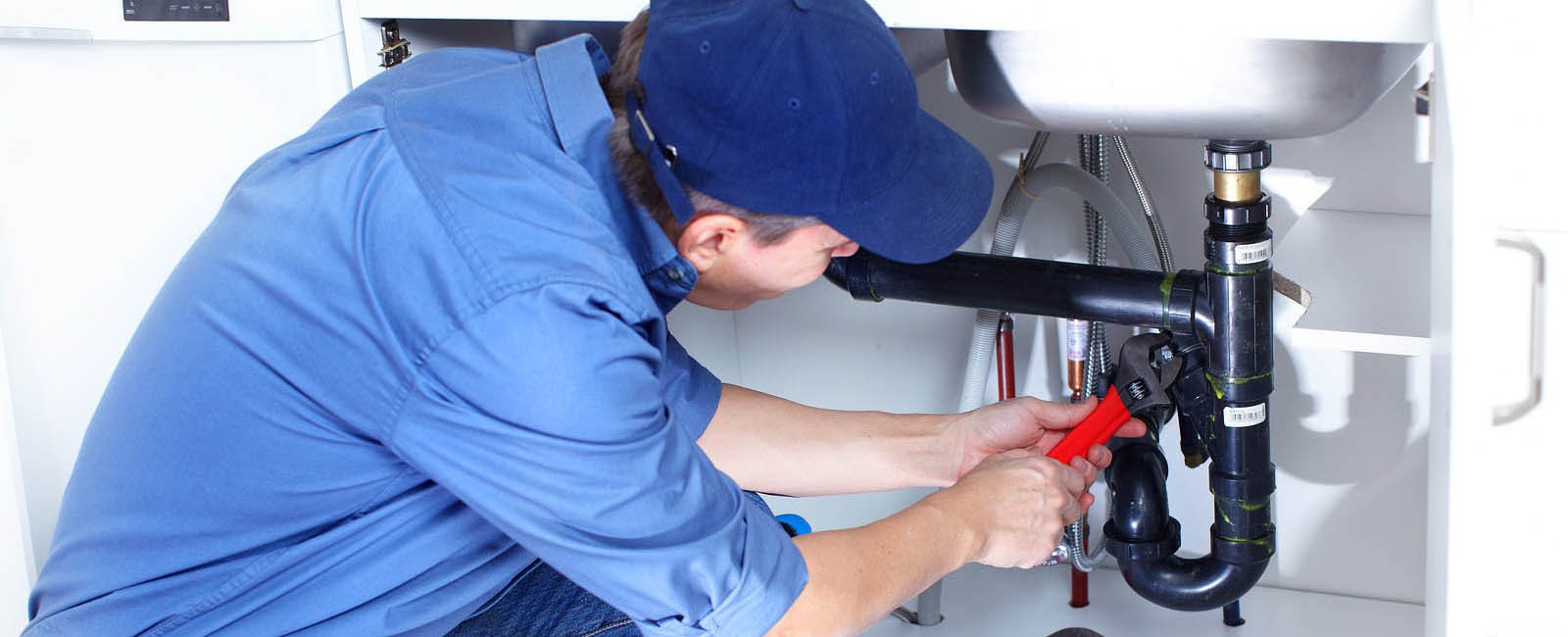 Mature plumber fixing a sink at kitchen