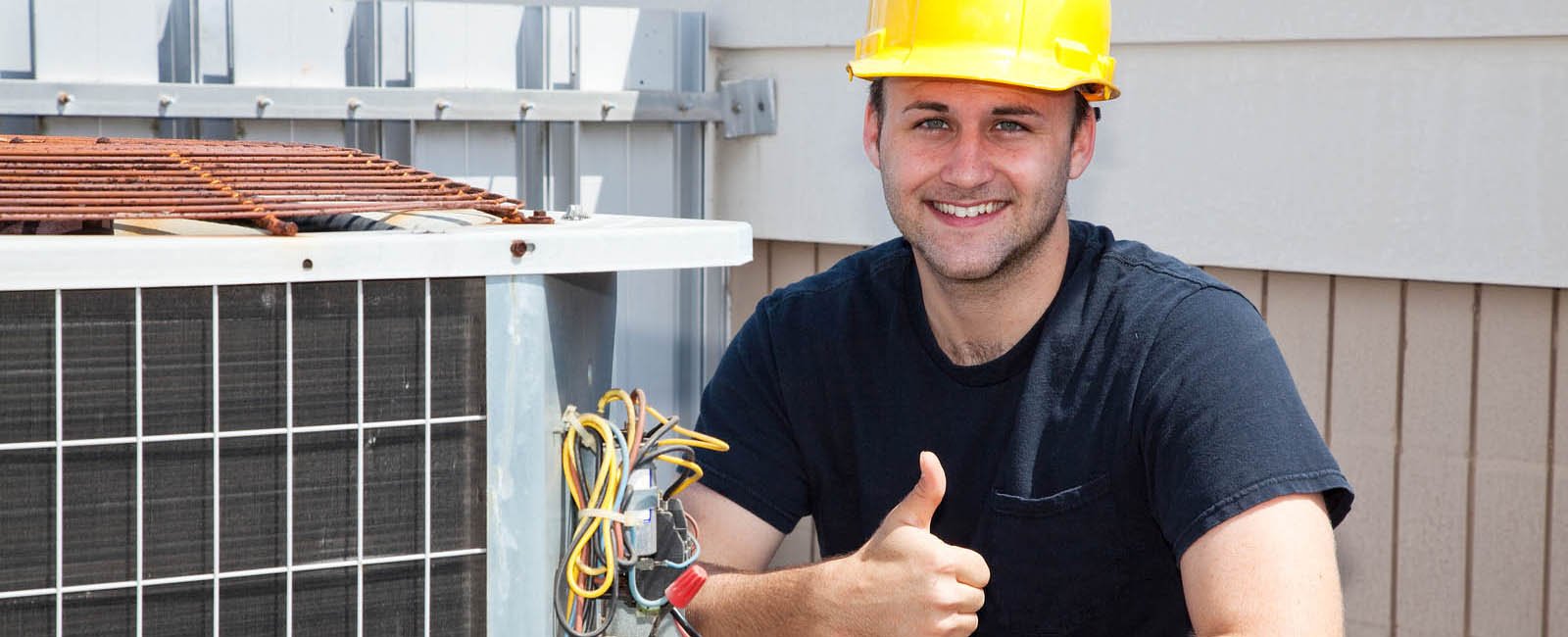 Air conditioning repairman working on a compressor and giving a thumbsup.